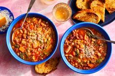 three bowls of chili and bread on a pink tablecloth with two glasses of beer