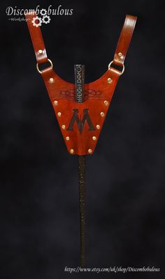 a red leather belt with gold rivets on the front and side, attached to a wooden stick