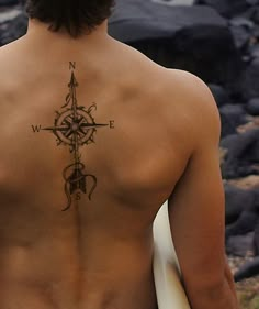 a man with a tattoo on his back holding a surfboard and looking at the ocean