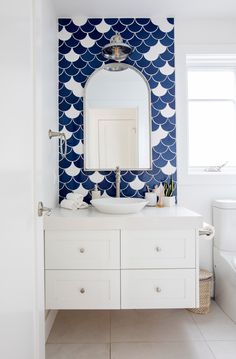 a white bathroom with blue and white wallpaper on the walls, sink and mirror