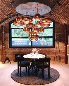 a round table with four chairs in front of a large window that has lights hanging from it