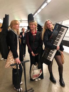 three women standing next to each other with musical instruments in their hands and one holding a bag