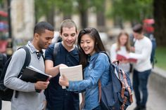 three people standing together and looking at a book in the middle of a city street