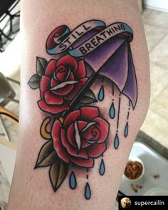 a woman's leg with an umbrella and roses tattoo on her thigh that says still breathing