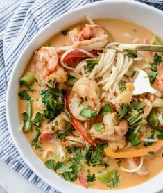 a white bowl filled with shrimp, pasta and veggies on top of a blue towel