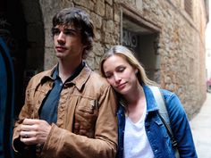 a young man and woman walking down the street in front of an old stone building