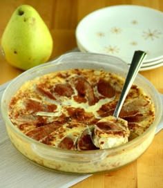 a pizza in a glass dish on a table next to two plates and a pear