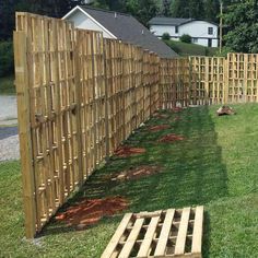 a fence made out of wooden pallets in the grass next to a yard with trees