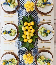 the table is set with yellow flowers and lemons on it, along with white plates