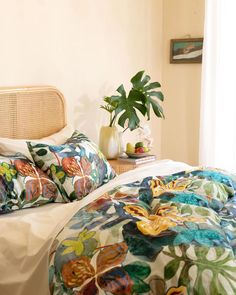 a bed with colorful comforters and pillows in a room next to a potted plant