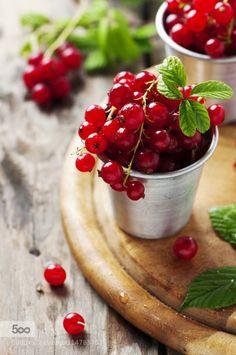 two small cups filled with cherries on top of a wooden tray next to leaves