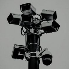 a black and white photo of several cameras attached to a street pole with the sky in the background