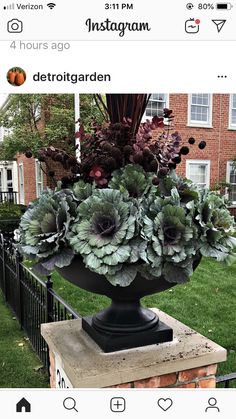 a large vase filled with lots of flowers on top of a brick block in front of a house