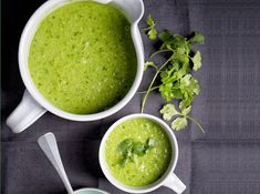 two white bowls filled with green soup and garnished with cilantro