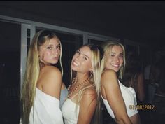 three beautiful young women standing next to each other in front of a window at night