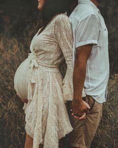 a man and woman holding hands while standing next to each other in tall grass with trees behind them