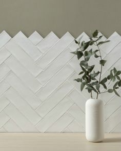 a plant in a white vase sitting on a table next to a wall with chevron tiles