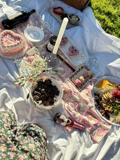 a picnic table with food and desserts laid out on the blanket in the grass