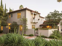 a large house with lots of plants in front of it and lights on the windows