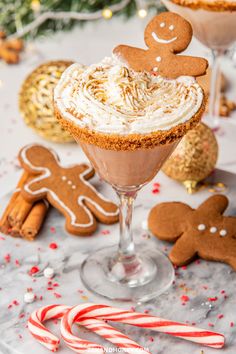 two glasses filled with hot chocolate and topped with whipped cream, gingerbreads and candy canes