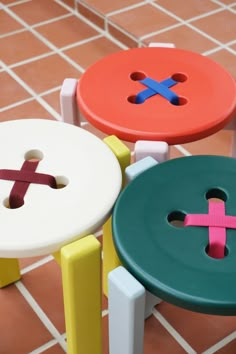 three colorful stools sitting on top of a tiled floor