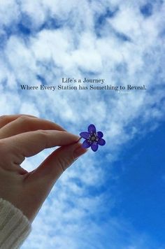 a hand holding a small purple flower under a blue cloudy sky with the quote life's a journey where every station has something to reveal