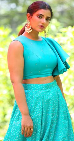 a woman with red hair wearing a blue top and skirt standing in front of trees