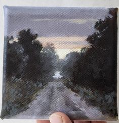 someone is holding up an oil painting of trees on the side of a road at sunset