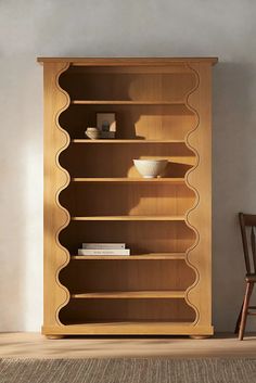 a wooden bookcase with three shelves and two chairs next to it in a room