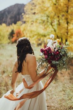 a woman in a white dress is holding a bouquet and looking down at the ground