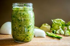 a jar filled with green sauce next to sliced cucumbers