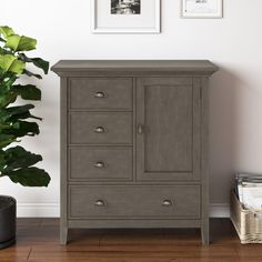 a grey cabinet next to a potted plant in a room with pictures on the wall