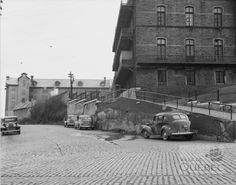 an old car parked on the side of a road next to a brick wall and stairs