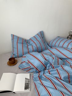 an open book on a bed with blue and red striped sheets, pillows and pillow cases