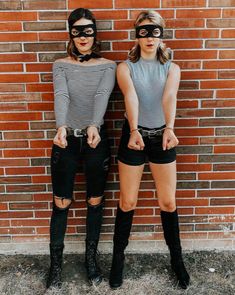 two women wearing masks standing next to a brick wall