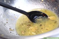 a metal bowl filled with yellow liquid next to a black spoon on top of it