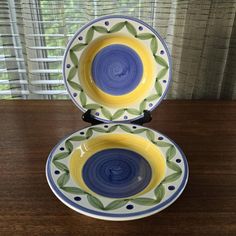 two yellow and blue bowls sitting on top of a wooden table next to a window