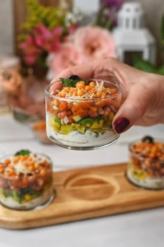 a person holding a small glass bowl filled with food on top of a wooden tray