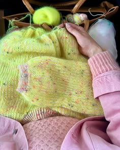 a person is laying down with some knitting supplies in their hand and there are two balls of yarn on top of the bag