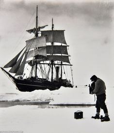 an old black and white photo of a man standing next to a boat in the snow