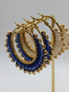 three pairs of gold and blue beaded hoop earrings on a metal stand against a white background