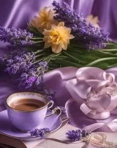 there is a cup of coffee and some flowers on the table with purple cloths