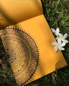 an open yellow book on the ground next to some white flowers and grass with one flower in it