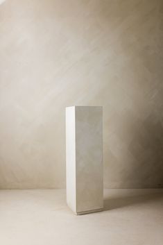 a tall white vase sitting on top of a floor next to a wall in a room