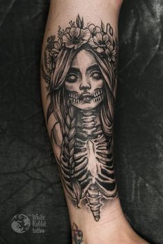 a woman's leg with a skeleton tattoo on it and flowers in her hair