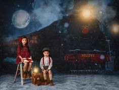 two children are sitting on stools in front of a train with the lights on