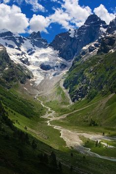 the mountains are covered in snow and green grass, with a river running between them