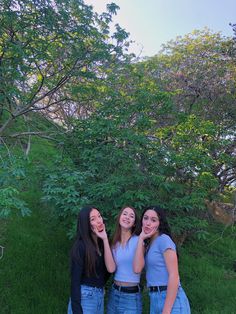 three young women standing next to each other in the grass