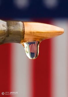 an american flag is reflected in the water droplet of a brass colored fountain faucet