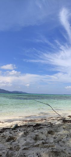 a boat sitting on top of a sandy beach next to the ocean under a blue sky